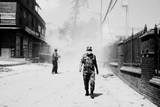 A soldier walks down a street with collapsed buildings in the background. Pashupatinath, May 3, 2015. JP/ Ayomi Amindoni