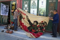 Vendors unfurl a banner from 1969 depicting former Chinese leader Mao Zedong as he "inspects the great army of the Cultural Revolution" and the slogan "Navigating the seas depends on the helmsman" at a curio market in Beijing, China, Monday, May 16, 2016. AP Photo/Ng Han Guan