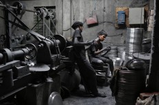 In this Sunday, June 12, 2016, photo, boys Imran, 11, left, and Nizam, 11, look at a mobile phone, as they take a break during their work at a factory that makes metal utensils in Dhaka, Bangladesh. AP Photo/ A.M. Ahad