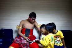 A wayang actor plays with his gadget alongside several children before the show begins. JP/ Wienda Parwitasari