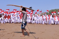 A surfer walks past a group of students carrying Indonesian flags on Baron Beach, Gunung Kidul, Yogyakarta. JP/Alb Magnus Kus Hendratmo