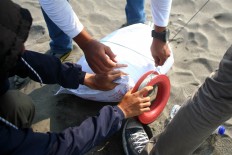 Two men tie the strings of a kite onto a rock. JP/ Aditya Sagita