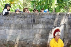 Muslim women living in a Muslim kampung in the middle of Bungaya village, take a peek over a wall at the Hindu ritual. About 20 Muslim men from Sasak Lombok joined the thousands of Hindu men to carry a mountain of produce, which can weigh between 2 to 7 metric tons. JP/ Luh De Suriyani