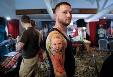 In this picture taken on Sunday, Oct. 16, 2016, Serghei, from the Republic of Moldova, poses with a fresh tattoo showing his son Chiril applied to his hand, during the International Tattoo Convention Bucharest 2016 in Bucharest, Romania. AP Photo/Vadim Ghirda