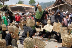 A participant with a bamboo helmet and shield signals the start of the tomato fight by dancing and throwing the first tomato. JP/Arya Dipa