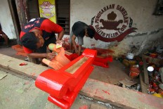 Workers paint a wooden rack for a bonang set red. JP/Aditya Sagita