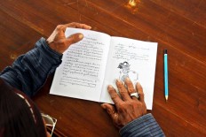 A servant opens a textbook on a page containing excepts of a wayang story. JP/ Aditya Sagita