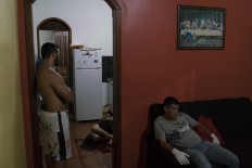 In this Feb. 5, 2017 photo, a gloved morgue worker rests at a home where the body of a woman lies on the kitchen floor after she was shot to death under unclear circumstances in Manaus, Brazil. The increasingly violent city is a thoroughfare for drug trafficking across South America, where authorities suspect most murders are gang related. AP Photo/Felipe Dana