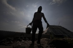 A woman carries a bucket of clay to be molded. She can mold up to 1,500 bricks per day.  JP/Sigit Pamungkas