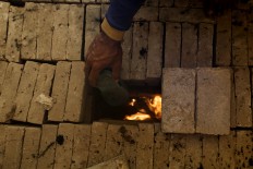 A craftsman puts an old rubber sandal and husk into a traditional stove to stoke a good fire with a high temperature for firing the bricks. JP/Sigit Pamungkas