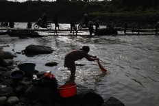 Life by the river: A villager washes clothes while motorists use semi-permanent bridge to cross the Cipamingkis river. JP/ PJ Leo