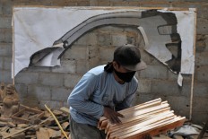 A worker carries a stack of wood planks that will be used in the replica. JP/Magnus Hendratmo