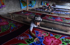 Rudi, 18, places finishing touches of color with a sponge on a beach sarong, while his fellow craftsmen attend to different stages of the wax-resist dyeing process at the Batik Satrio workshop in Senepo Rejo village. JP/Aman Rochman