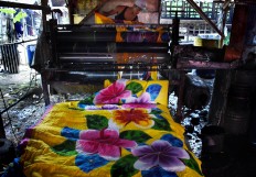 A craftsman feeds lengths of dyed fabric through a roller to press and flatten them. JP/Aman Rochman
