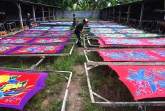 Three men stretch lengths of dyed sarong on wooden frames to dry and shape them under the sun. JP/Aman Rochman