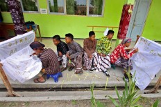 Two male students create batik while their classmates look on. JP/Aditya Sagita