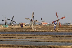 A farmer repairs a windmill, while his colleagues are working on the field. Antara/Dedhez Anggara