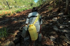 An old woman carries two jerrycans filled with water on her back to bring them home. JP/Aditya Sagita