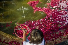 A young girl throws red rose petals into a pond in the middle of the monument. JP/Anggara Mahendra