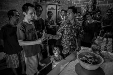 One for one: Imanuel Talan distributes slices of watermelon to residents while his daughter, 2-year-old Senandung Nathania Talan, watches. JP/Seto Wardhana