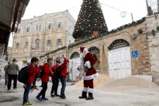 A man dressed as a Santa Claus greets children near a giant Christmas tree, as he walks in the Christian Quarter of the old city of Jerusalem on December 20, 2017. AFP/Gali Tibbon