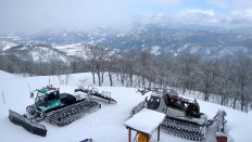 Two snow excavators stand idly with Japan’s Northern Alps in the background. JP/Agnes Anya