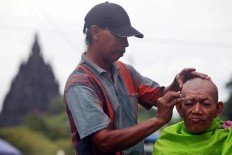 nice view: Widodo cuts the hair of a customer against the backdrop of the Prambanan temple. JP/ Boy T Harjanto