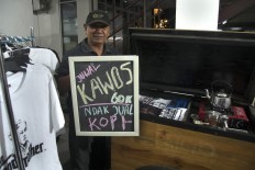 A seller shows his promotional board saying “Juwal kawos ndak jual kopi”, which means he sells T-shirts instead of coffee. JP/Tarko Sudiarno