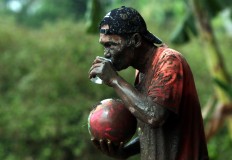 A player with his face covered in mud drinks a glass of water. JP/Boy T. Harjanto