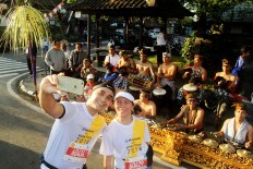 Musical sideline: Two runners pose for a selfie in front of a traditional Balinese orchestra during the 2018 Maybank Bali Marathon on Sept. 9 in Gianyar, Bali. The international race also seeks to promote Balinese culture.