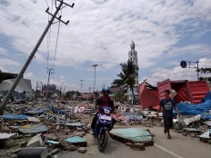 Residents make their way along a street full of debris after an earthquake and tsunami hit Palu, on Sulawesi island on September 29, 2018. Rescuers scrambled to reach tsunami-hit central Indonesia and assess the damage after a strong quake brought down several buildings and sent locals fleeing their homes for higher ground.   AFP/ Muhammad Rifki