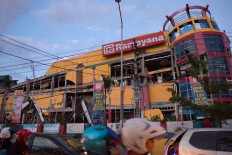 Motorists drive past a collapsed shopping mall in downtown Palu, Indonesia's Central Sulawesi on September 30, 2018, following the September 28 earthquake and tsunami. The death toll in Indonesia's quake-tsunami disaster nearly doubled to more than 800 on September 30, as ill-equipped rescuers struggled to reach scores of trapped victims, health officials resorted to mass burials and desperate residents looted shops for food and water. AFP/ Bay Ismoyo