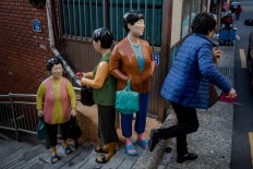 An elderly woman passes by statues on a staircase. JP/Anggara Mahendra