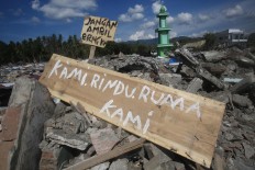 Signs have been placed in the middle of the debris of tumbled houses. One of the signs reads “Kami rindu ruma kami” (we miss our home). JP/Dhoni Setiawan