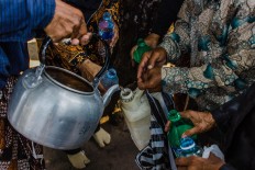 A courtier uses a kettle to distribute sacred water among the public. JP/Anggertimur Lanang Tinarbuko