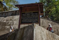 Two women walk pass by board detailing the rules of attending the Nguras Enceh ritual. JP/Anggertimur Lanang Tinarbuko