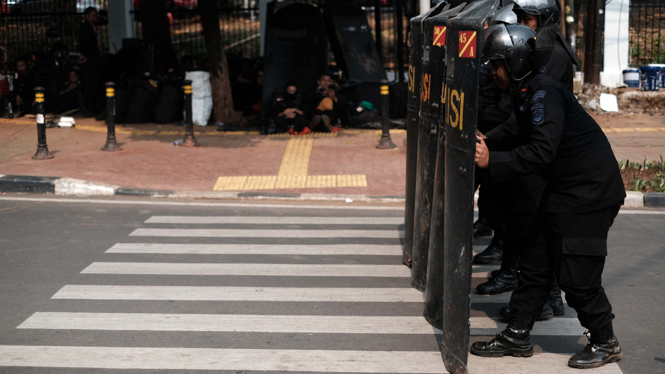 Several Mobile Brigade (Brimob) members hold up their shields as other members rest under the shade of sidewalk trees behind the House of Representatives building in Senayan, Jakarta, on Thursday. Security members secured the area for the inauguration of the President and Vice President for the 2019-2024 term on Sunday. JP/P.J.Leo