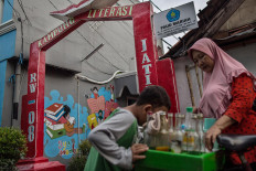 A boy looks at the wares of a jamu (herbal drink) seller in front of the archway to the Jatipulo literacy kampung in West Jakarta. JP/Afriadi Hikmal