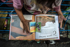 Aini flips through superhero character cards amid pages on desert geography in the Jatipulo literacy kampung. JP/Afriadi Hikmal