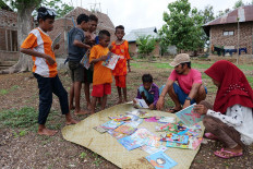 Muhammad Ridwan Alimuddi (second right), the founder of the Armada Pustaka Mandar program, watches as children select books from a mat on Pantar Island in East Nusa Tenggara. JP/ Yusuf Wahil