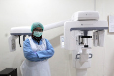 A radiologist wears a mask and protective suit while operating a dental X-ray machine. JP/Fauzan
