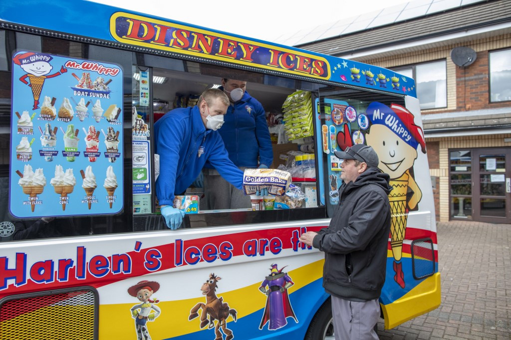Workers sell food and household items from their ice cream van to local residents at a supported housing estate in west Belfast on April 1, 2020 after they turned their van into a mobile mini-market selling essential items to residents who are trapped at home by the coronavirus outbreak. 