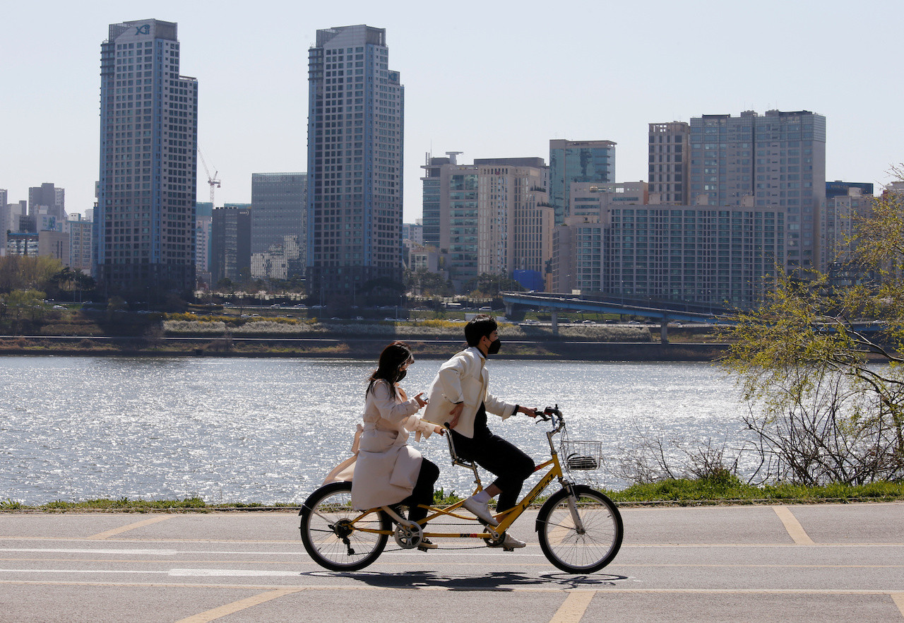 A couple wearing masks to protect against contracting the coronavirus disease (COVID-19) ride on a bicycle at a Han River Park in Seoul, South Korea April 4, 2020. 