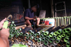 Sukri (left) inserts a ripe banana leaf and a young banana leaf into a bamboo tube. Meanwhile, his son Junet (center), pours glutinous rice into a tube.  JP/P.J. Leo