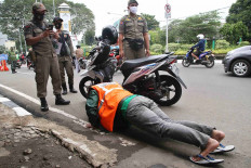 A Public Order Agency (Satpol PP) officer takes a picture of a motorist who does pushups as a punishment for violating the large-scale social restrictions (PSBB) in Depok, West Java, on May 19. Punishments for offenders of the PSBB range from pushups and singing the national anthem to sweeping the streets. JP/P.J. Leo

