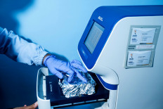 A laboratory worker inserts swab specimens into the tray of a real-time polymerase chain reaction (PCR) machine. JP/Agung Parameswara