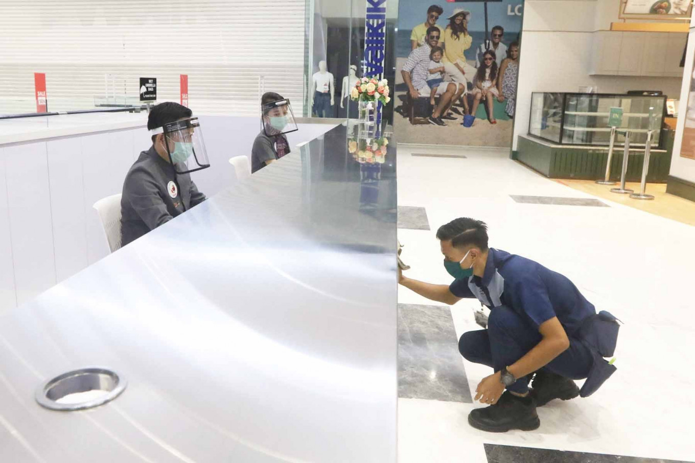 Receptionists wear face shields and masks on Wednesday during their shift at a shopping mall in West Jakarta, as a cleaner in a face mask goes about his task. According to a study conducted by Nielsen Indonesia, only 67 percent of regular shopping malls visitors were interested in coming back during the PSBB relaxation period or the so-called new normal.