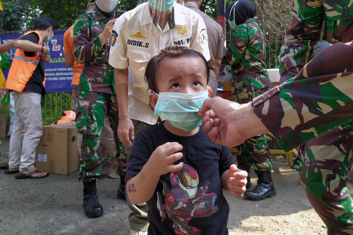 A soldier helps a boy put on a face mask during an event to mark the transitional period of large-scale social restrictions (PSBB) in East Jakarta on June 26. The boy was with his father (back, left), who was found violating PSBB measures and ordered to sweep the area as punishment.