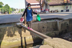 A woman carefully crosses a makeshift bridge placed over a gutter behind the Kampung Rambutan bus terminal in East Jakarta on July 1. The bridge lead to the terminal&rsquo;s back gate. Some commuters prefer this precarious path as it is closer than the terminal&rsquo;s main gate. JP/P.J.Leo