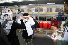 A woman helps her son put on a mask and face shield before they board the Argo Parahyangan train at Bekasi station in West Java on July 10. State-owned train operator PT Kereta Api Indonesia (PT KAI) has added long-distance train services to cater to travelers going to and from Greater Jakarta. JP/P.J.Leo